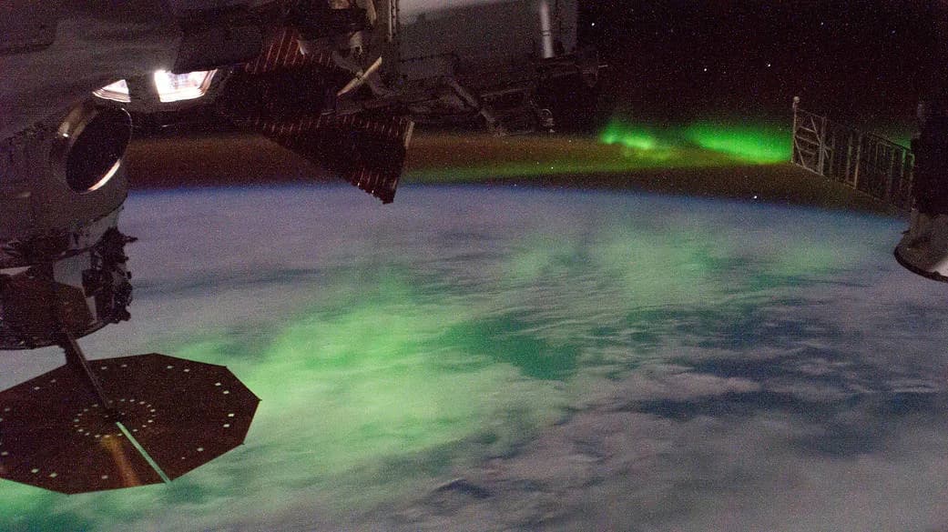 The aurora australis glowing green above Earth's curved horizon at night