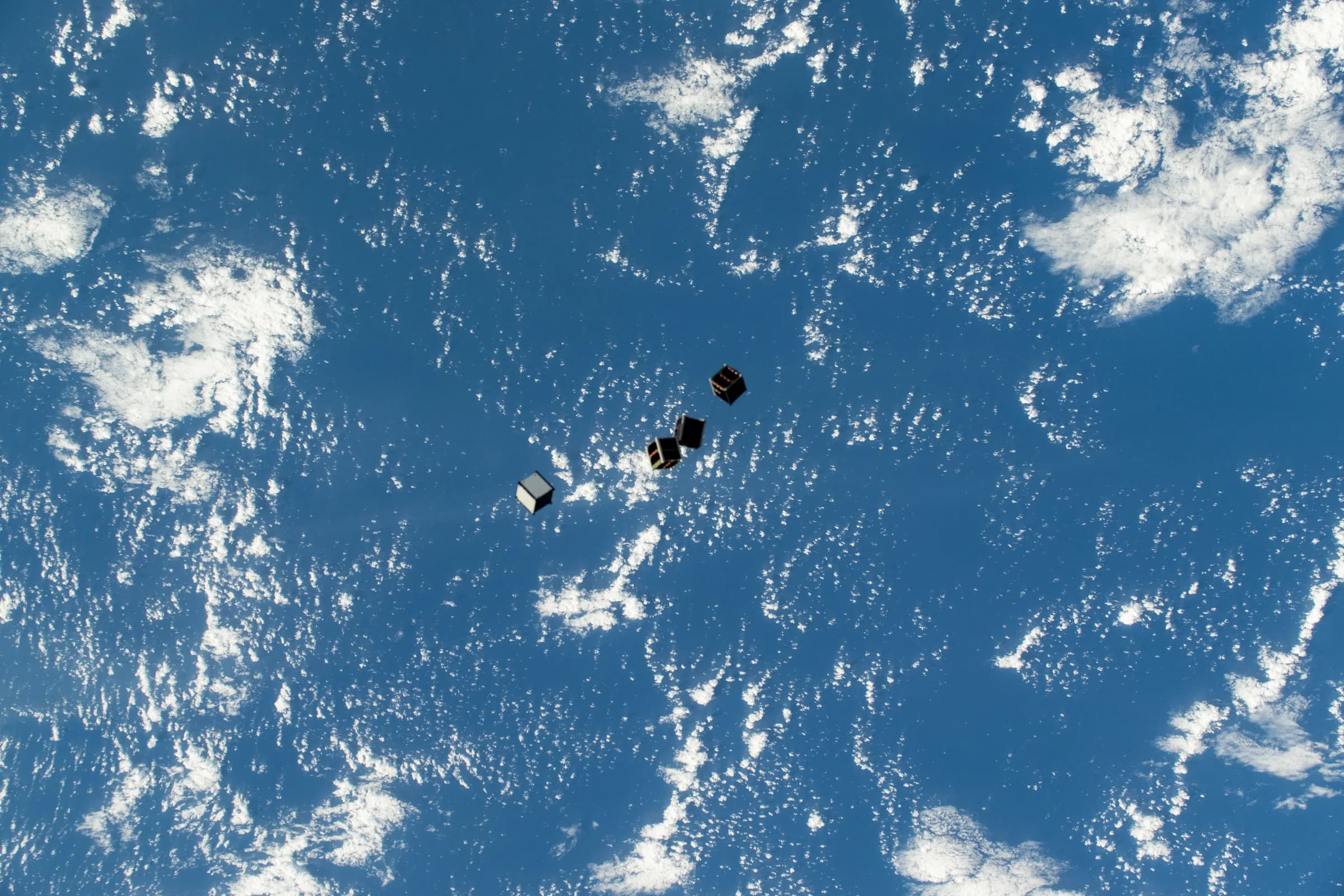 Four small CubeSats drifting above the blue ocean after deployment into Earth orbit